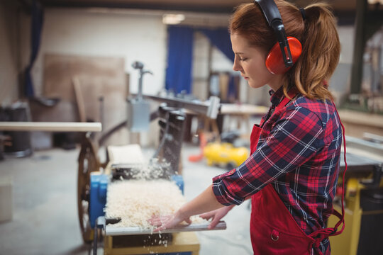 Woodworking planer producing fresh shavings while feeding board through machine at workshop bench