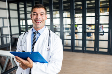 Doctor standing in healthcare corridor holding blue clipboard with stethoscope around neck