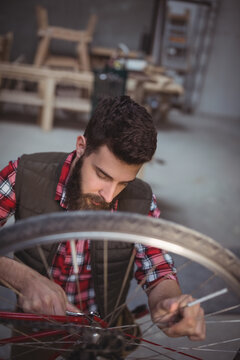 Bicycle mechanic tightening hub on bicycle wheel in workshop, with tools on metal shelving