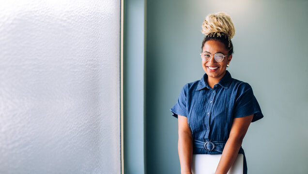 Smiling black businesswoman standing near window holding a laptop