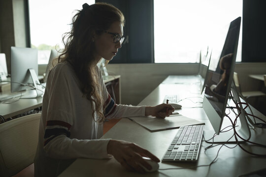 Teenage girl taking notes while using computer at school lab with monitor and notebook, copy space - Powered by Adobe