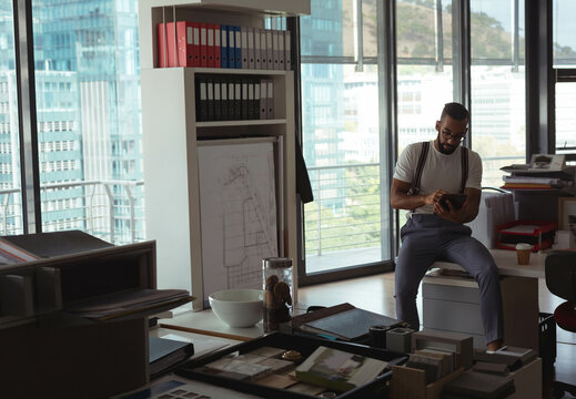African American man using tablet at design studio desk with binders and sample boards, copy space
