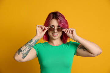 Beautiful woman with pink dyed hair in sunglasses on yellow background
