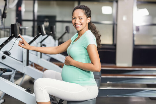 Mid adult pregnant woman wearing mint green top using rowing machine display console at gym