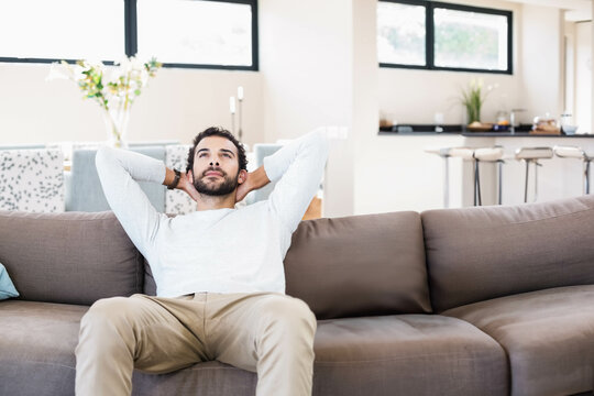 Man relaxing on gray sofa in open-plan living area near dining table with white flowers