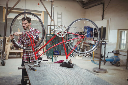 Fototapeta Bike mechanic tightening bolts on upside-down red bicycle at metal workbench in industrial workshop