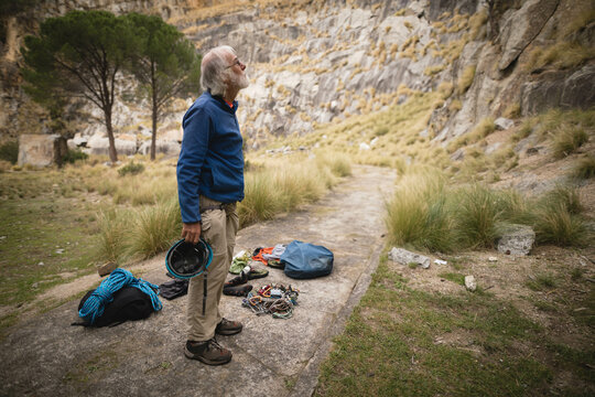 Senior man preparing climbing gear on slab at canyon base with helmet rope carabiners, copy space