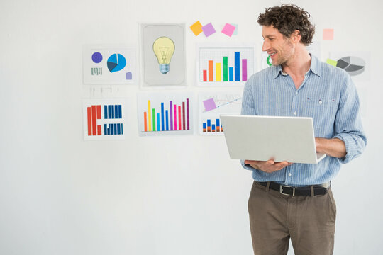 Silver laptop displaying bar graphs pie chart and line graph against white wall, with sticky notes