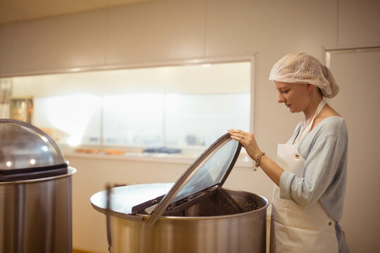 Female food processing worker lifting lid of stainless steel vat in industrial kitchen, copy space