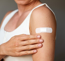 Closeup white adhesive bandage on female's shoulder after vaccine shot