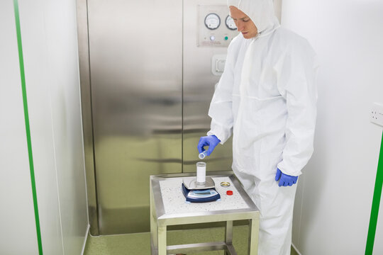 Male lab tech wearing protective gear pouring powder into vessel on scale in cleanroom, copy space