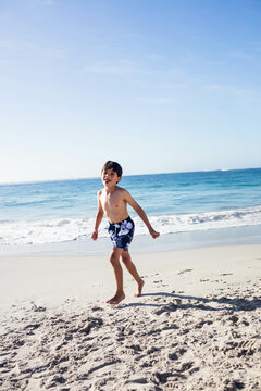Gentle ocean waves lapping onto beige sand along beach under clear sky with footprints, copy space
