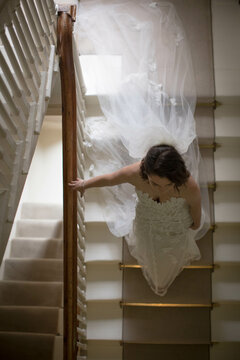 Bride climbing carpeted staircase using banister over brass rods with lace gown and veil