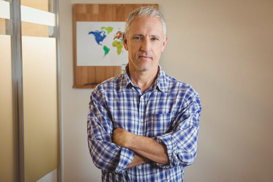 Senior man standing with arms crossed in office with frosted glass partition and world map print