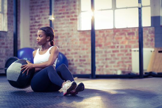 Female holding medicine ball twisting torso in gym near stability balls and squat rack, copy space