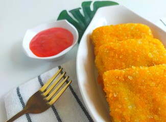 Close-up of crispy fried mayonnaise risoles filled with ham, egg, and cheese, served on a wooden board with a small bowl of pink dipping sauce. Risol mayo.