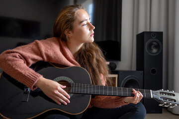 Teenage girl playing guitar at home. Guitar. Stringed musical instrument.