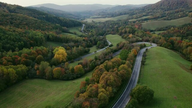 Drone shot of national park, asphalt road in a valley, hills in background, autumn sunset