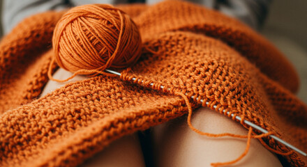 Fototapeta premium Cozy knitting project with orange yarn on lap in relaxed setting 