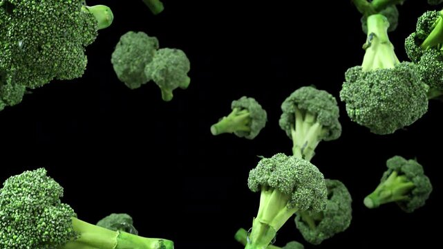 Close-up of broccoli florets falling in slow motion on black background, crisp texture and vivid green color.