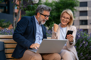 Excited professional people celebrating success outdoors in business district, holding laptop, cheering for SEO achievement and design agency win, diverse team in corporate area