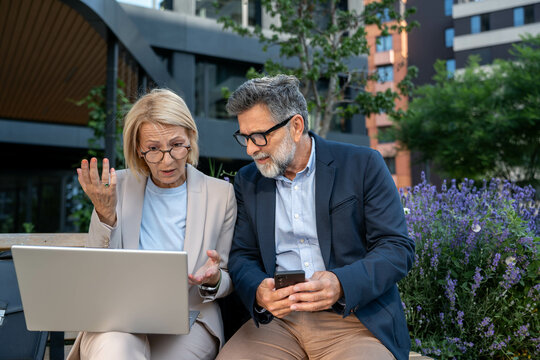Disappointed and worried businessman and businesswoman in business district looking at laptop, reacting to bad news about failed project, corporate stress and concern