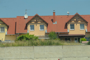 A long row of houses featuring satellite dishes mounted prominently on their roofs, adding to the...