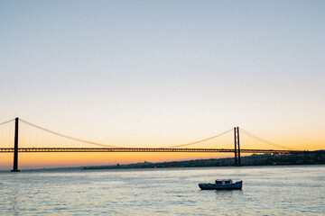 25 de Abril Bridge at Sunset with Boat on Tagus River – Lisbon, Portugal