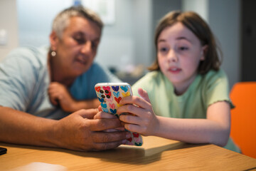 Smiling caucasian grandmother and  granddaughter enjoying time together with smartphone. 