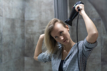 Young woman enjoying her morning routine while drying her long blond hair with a hair dryer in a sleek, modern bathroom, surrounded by clean tiles and a fresh atmosphere