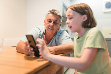 Obraz premium Smiling caucasian grandmother and granddaughter enjoying time together with smartphone. 