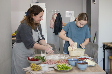 Attractive child girl daughter and mother preparing dough for pizza and smiling while baking in kitchen at home, family together
