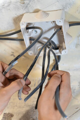 Electrician carefully connecting electrical wires to a junction box on a ceiling during a home renovation, ensuring safe and reliable electrical connections. Vertical photo
