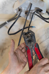 Electrician is working on electrical wiring, using wire strippers to carefully prepare wires for connection to a junction box during a home renovation or construction project. Vertical photo