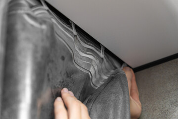 Close-up view of hands installing grey striped curtains on a ceiling track, highlighting the intricate process of home decoration in a modern, stylish living space