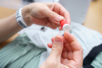 Hands thread a needle with red thread for sewing a garment during a craft session in a bright indoor space