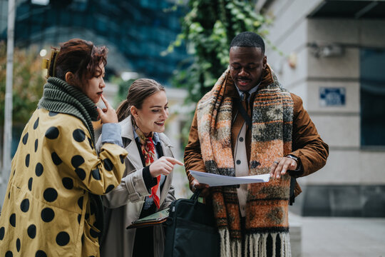 Group of multiracial business people collaboratively working on ideas while reviewing documents outdoors. They appear excited and engaged as they exchange thoughts, showcasing teamwork and creativity.