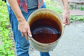 man in blue jeans holding dirty round industrial plastic garden white bucket with iron handle with water in hands during daytime on street