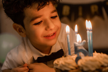 handsome little curly-haired brunette boy makes a wish and blows out the candles on the cake