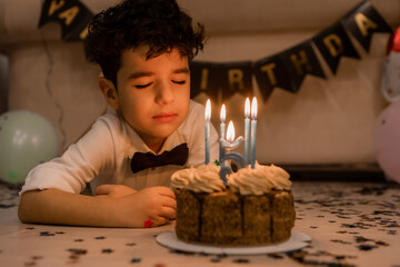 handsome little curly-haired brunette boy makes a wish and blows out the candles on the cake