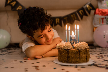 handsome little curly-haired brunette boy makes a wish and blows out the candles on the cake