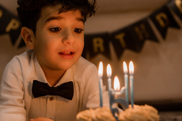 handsome little curly-haired brunette boy makes a wish and blows out the candles on the cake