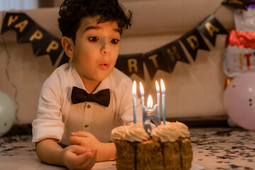 handsome little curly-haired brunette boy makes a wish and blows out the candles on the cake