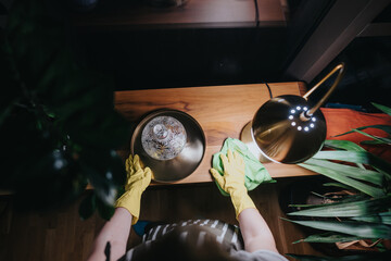 A nighttime housekeeping routine featuring someone wearing rubber gloves, meticulously cleaning a wooden desk adorned with an artistic decorative bowl and glowing lamp.
