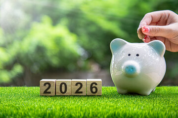 Financial coins stacked with wooden cubes of the year 2026 on a natural background. Piggy bank. New Year 2026 is about finances and saving money.
