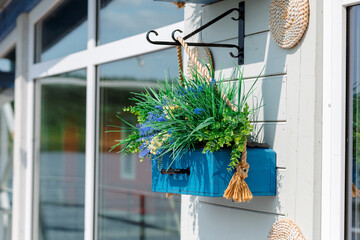 A bright blue flower box, suspended from a metal hook, is decorated with greenery and flowers, creating a cozy and stylish accent on the facade.