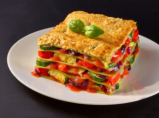 Gemueselasagne auf weissem Teller auf schwarzem Fond, italien, Käse überbacken, 