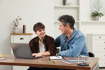 Obraz premium Smiling father and his son doing homework with laptop at table indoors
