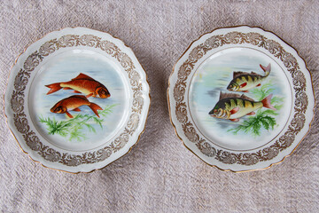 High angle view of two vintage oval porcelain dinner plates with painted fish and scalloped rim set...