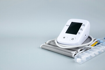 Digital blood pressure tonometer and pack of pills on a blue background with copy space.